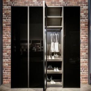 Auch dieser Drehtürenschrank von © raumplus ist mit seinen schwarzen Glastüren eine elegante Erscheinung und sieht sehr cool aus vor dieser Ziegelwand.